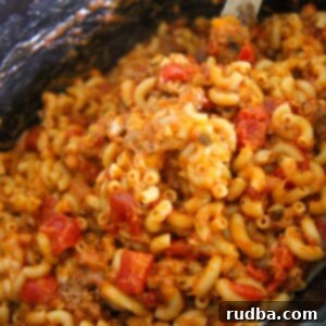Hearty Slow Cooker Cheesy Beef Goulash 2 Crockpot cheesy beef goulash with a wooden spoon.
