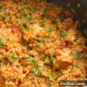 Creamy Cuban Chicken and Rice 2 arroz con pollo a la chorrera up close. A vibrant, rich yellow soupy rice with chicken pieces and green peas in a large bowl.