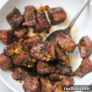 garlic butter steak tips on a white plate with a spoon.