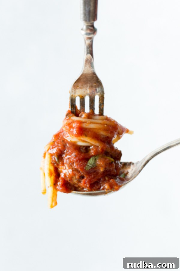 A spoon holding a small portion of spaghetti and a meatball with a fork on top.