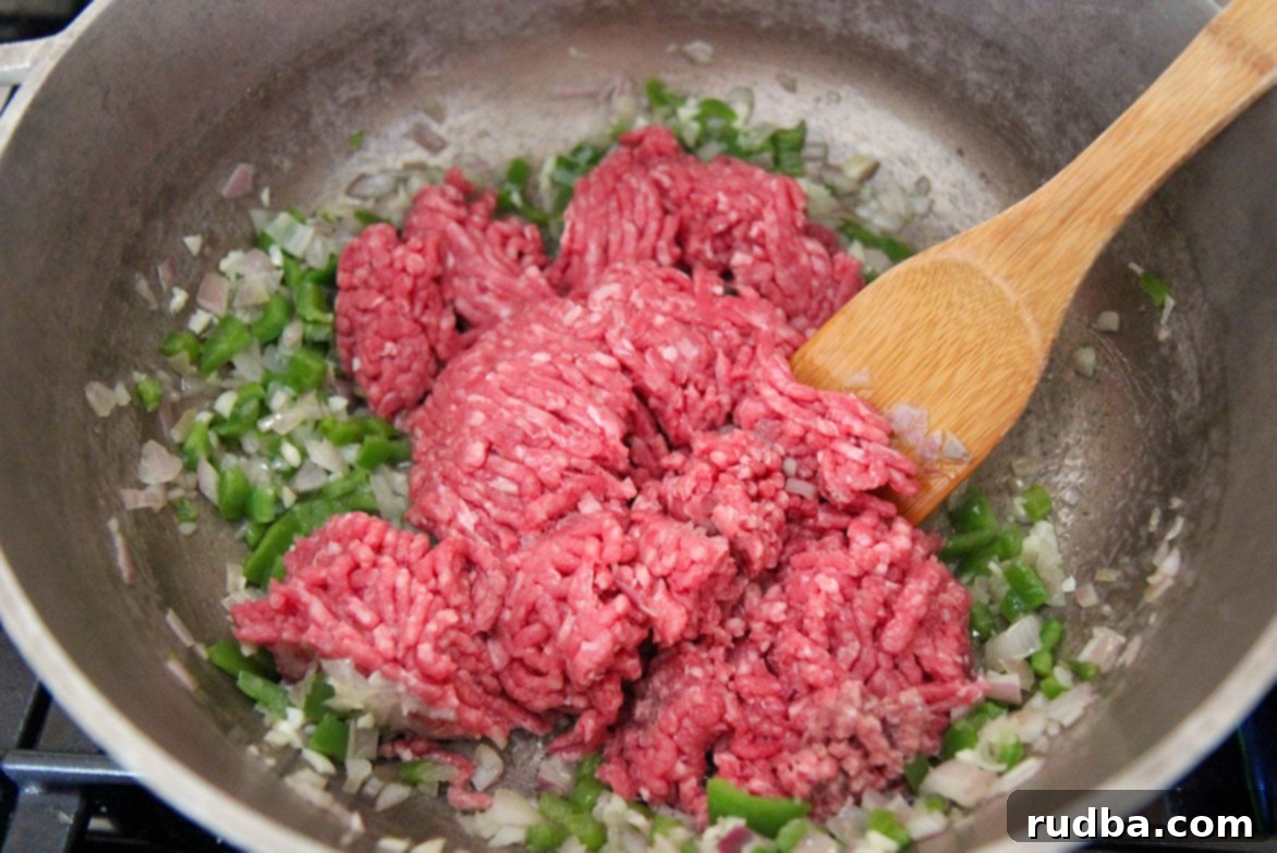 onions, peppers, and ground beef in a skillet with a spoon