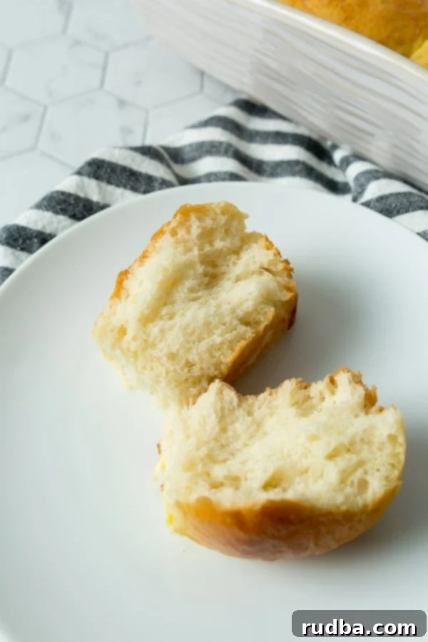 One bread roll split in half on a small white plate with a blue and white patterned kitchen towel on the side, highlighting its soft, fluffy interior.