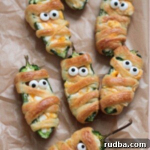 Mummy jalapeno poppers on parchment paper.