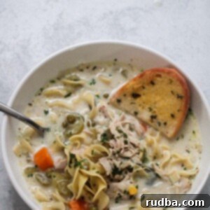 Velvety Instant Pot Chicken Noodle Soup 2 creamy chicken noodle soup in a bowl with a spoon and slice of garlic bread.