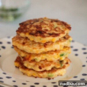 Golden Corn Fritters 2 Stacked golden corn fritters on a plate, garnished with fresh herbs.
