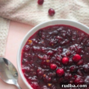 Timeless Cranberry Companion 2 classic cranberry sauce in a bowl with a spoon, towel, and cranberries on the side.
