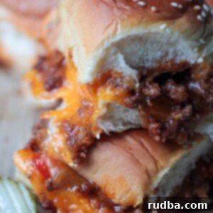 two sloppy joe sliders stacked on a wooden board with a pickle on the side.