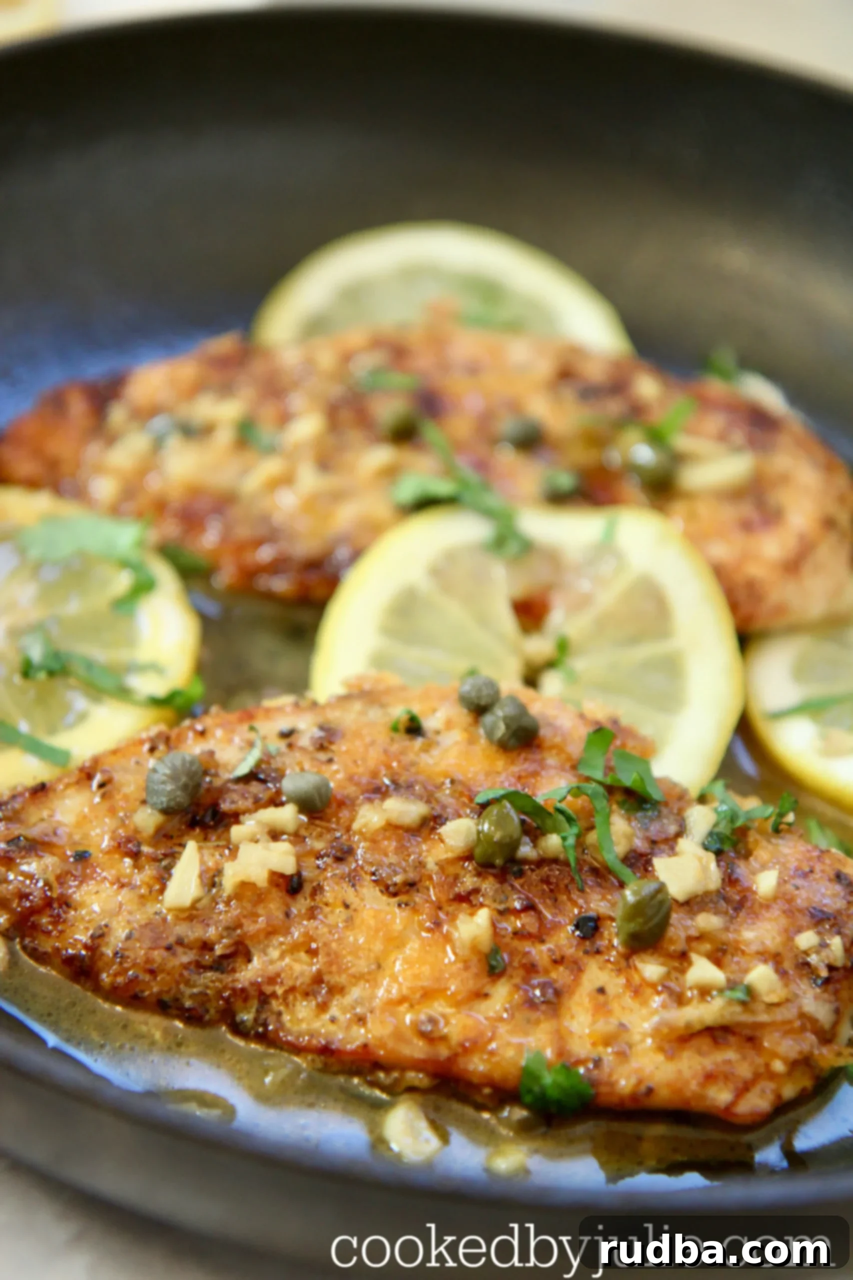 chicken in a skillet with sauce, capers, lemons, and parsley. 