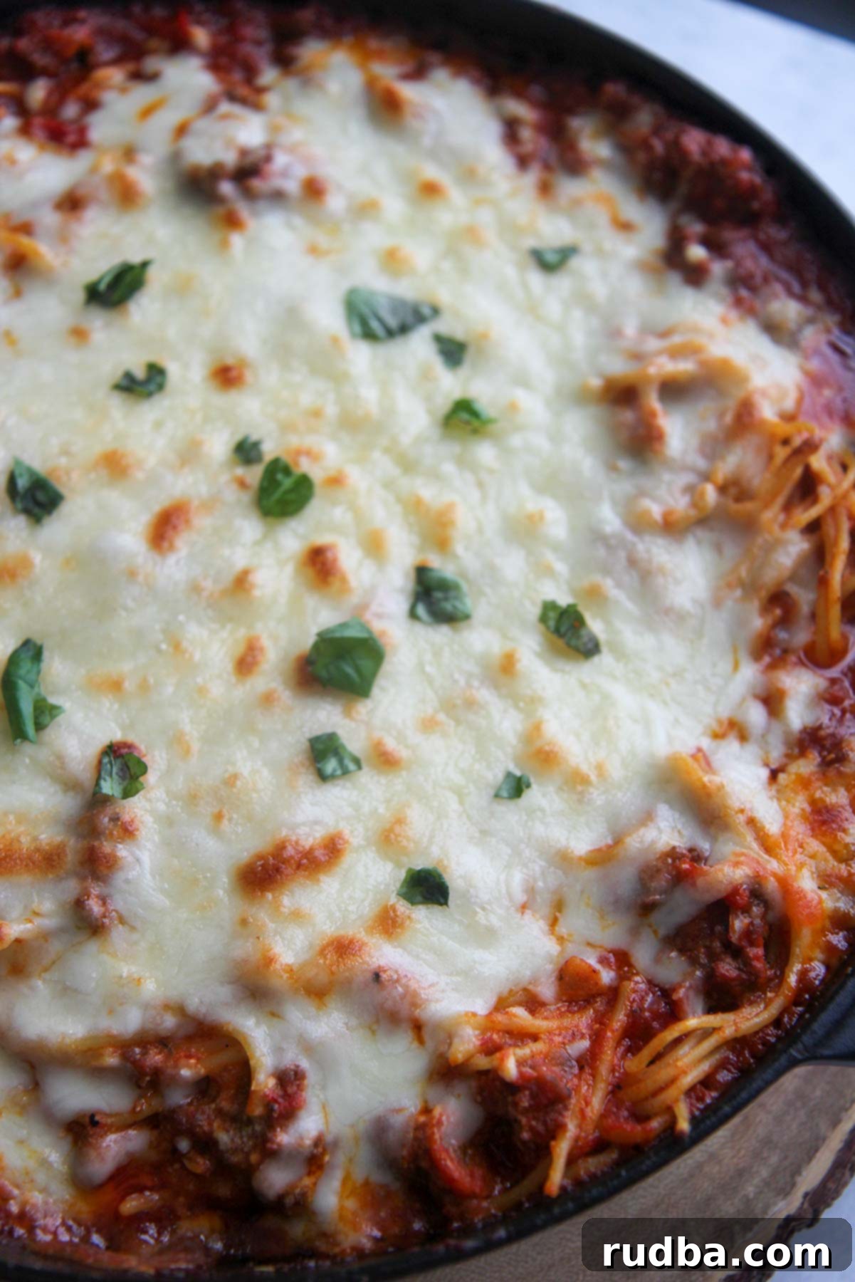 Close-up of baked spaghetti with melted, bubbly cheese, garnished with fresh basil.