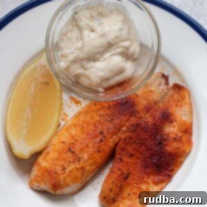 Crispy Air Fryer Tilapia 2 air fryer tilapia with tartar sauce and a lemon wedge.