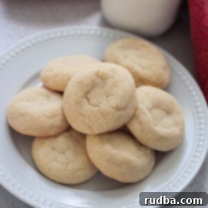 Sugar Cookies 2 sugar cookies on a white plate with a red towel and milk in the background.