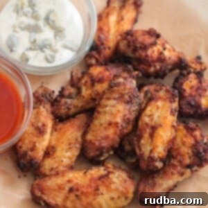 air fryer chicken wings on a plate with buffalo sauce and blue cheese dressing on the side.