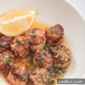 Pan-Seared Scallops with Lemon Butter 2 lemon butter scallops on a white plate with a lemon wedge on the side.