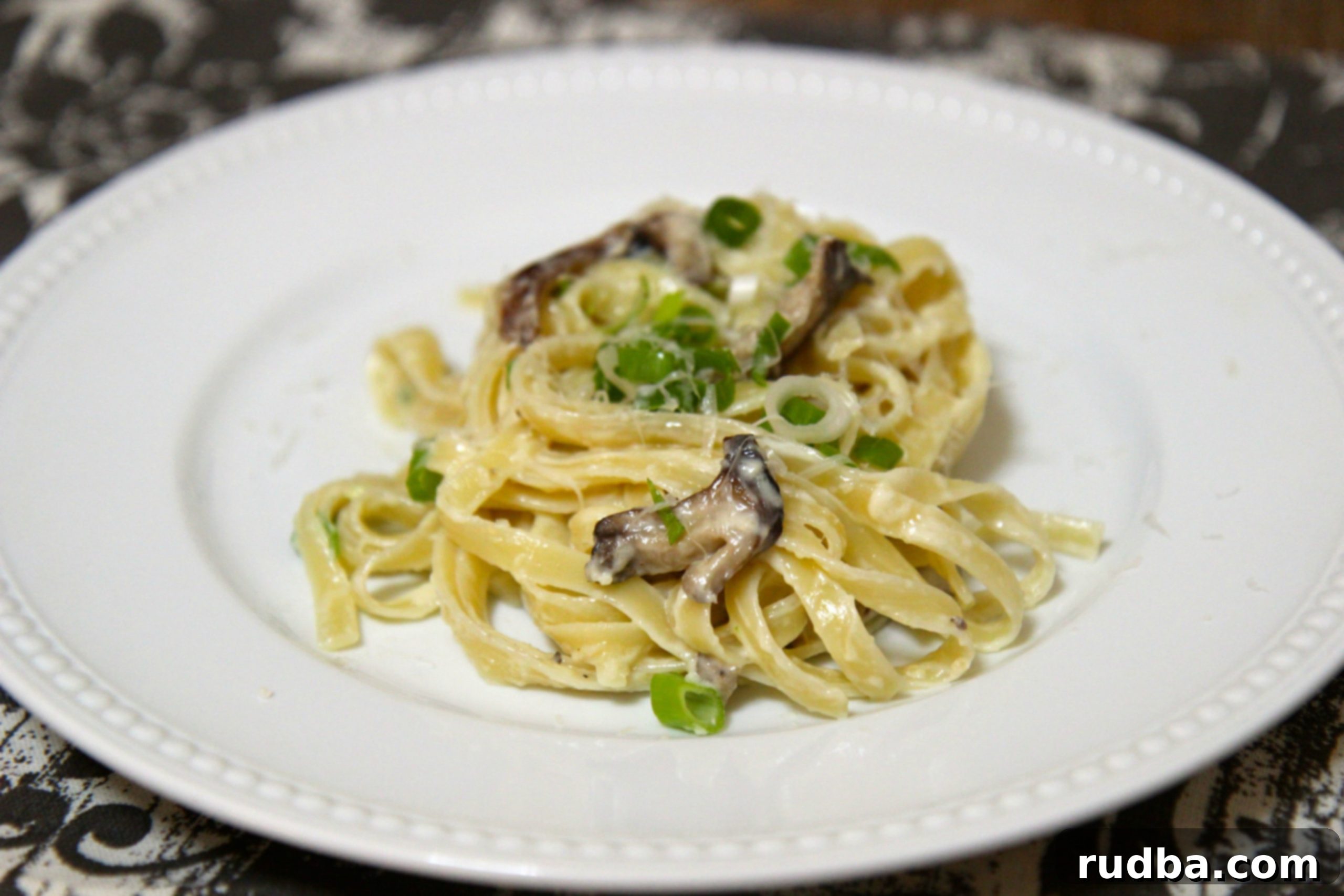 Al Dente pasta in a creamy alfredo sauce with mushrooms and green onions, served on a plate
