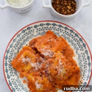 lobster raviolis and sauce on a plate with parmesan cheese and red crushed pepper on the side.