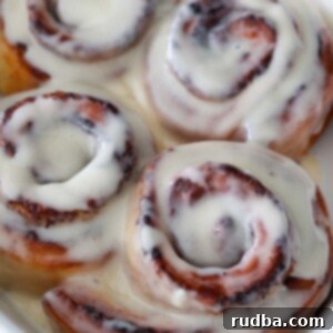 Golden Air Fryer Cinnamon Rolls 2 air fryer cinnamon rolls with cream cheese icing on top.