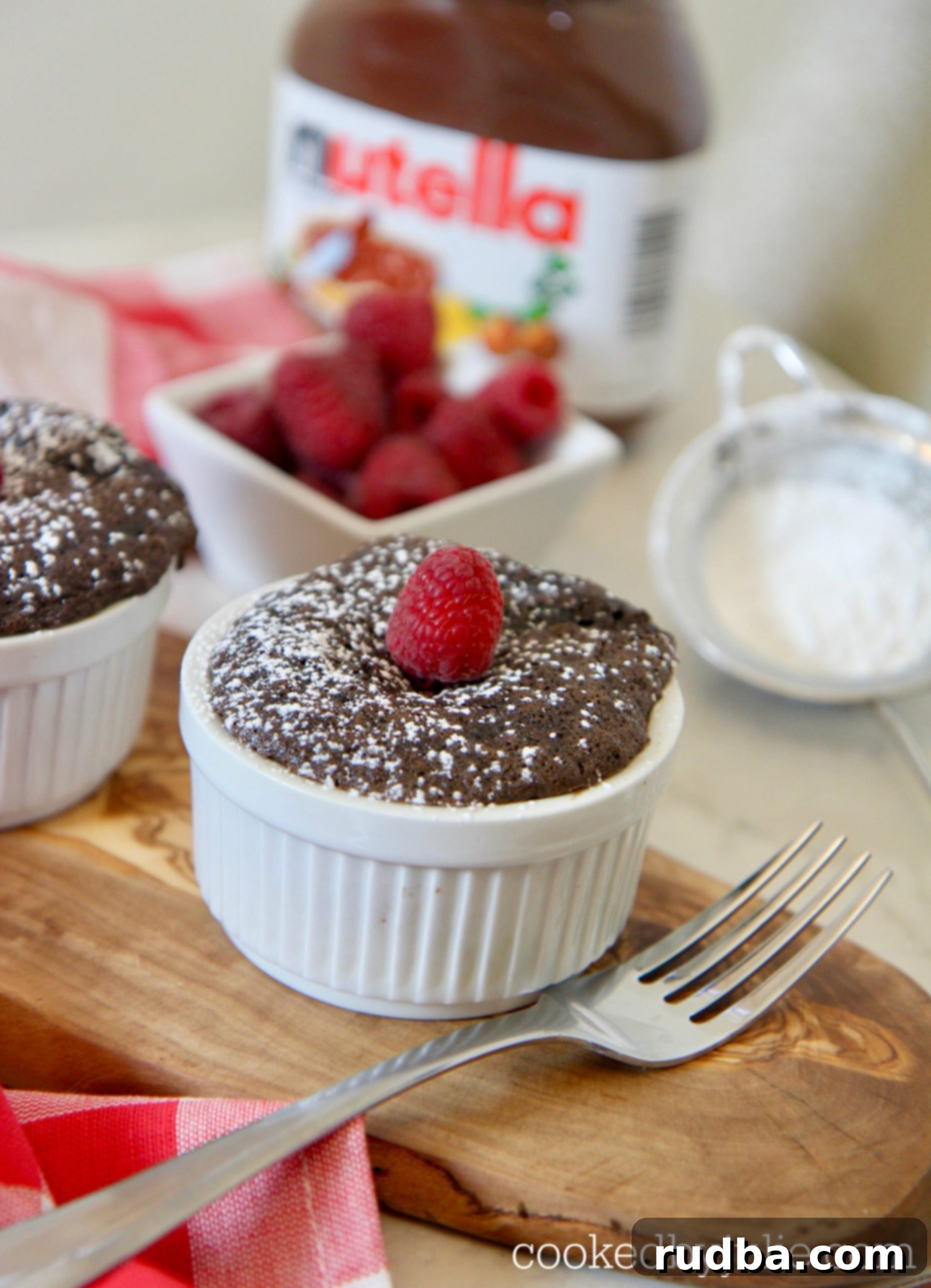 chocolate Nutella cake in a ramekin with powdered sugar and fresh raspberries.