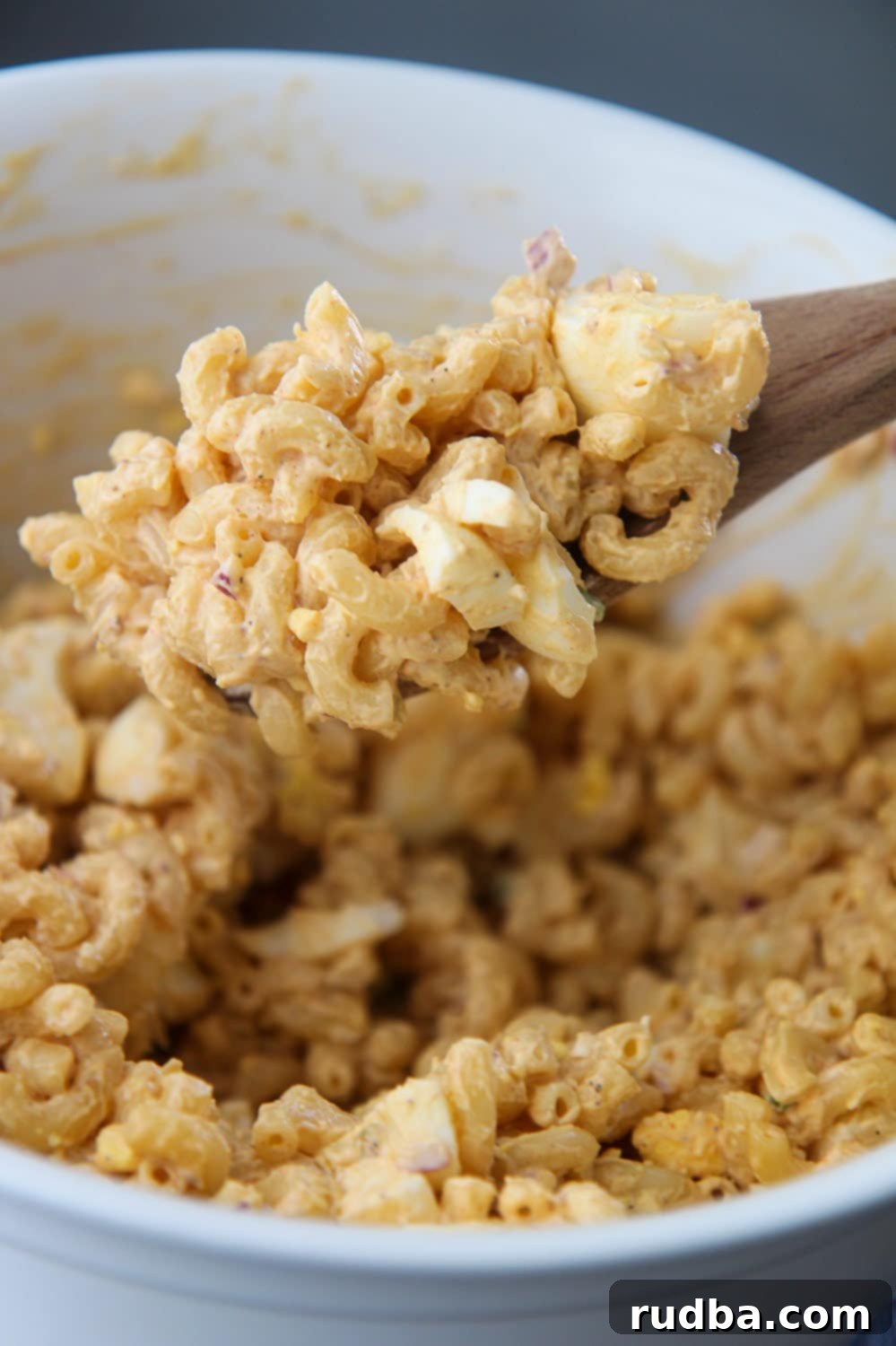 Elbow macaroni with hard boiled eggs and a wooden spoon, ready for mixing.
