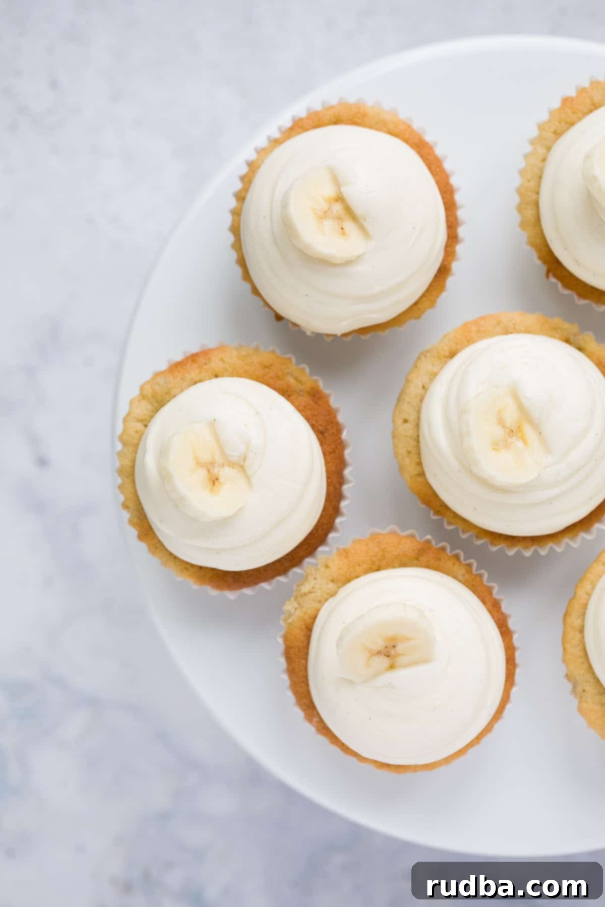 six banana cupcakes with cream cheese frosting on a cake stand