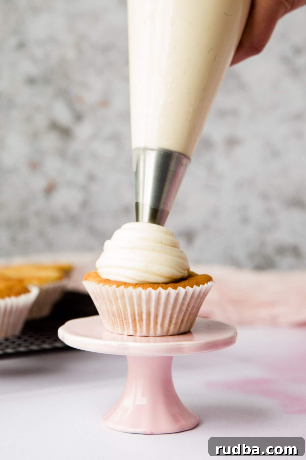 a cupcake being frosted with a piping bag and star tip.