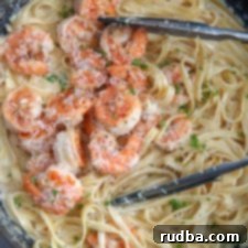 Irresistible Shrimp Creations 13 Shrimp over fettuccine alfredo in a black skillet with tongs and fresh parsley.