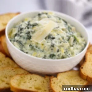 Crockpot spinach artichoke dip in a white bowl with baguette slices.