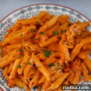 Penne Alla Vodka on a plate, garnished with fresh herbs and Parmesan.