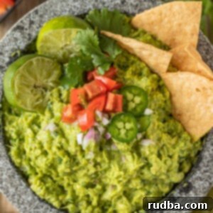 Guacamole 2 Guacamole in a molcajete topped with limes, tomatoes, jalapenos, and chips.