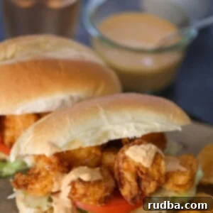 Two crispy shrimp po'boy sandwiches on a wooden board with chips and a pickle on the side.