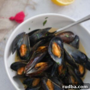 Mussels in Lobster Nectar 2 black opened mussels with a spoon in a white bowl with a lemon on the side.
