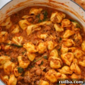 Creamy cheese tortellini with spinach and savory meat sauce in a large pot, ready to be served.