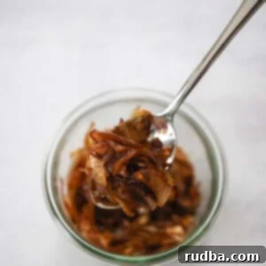 A small white bowl filled with perfectly caramelized onions, with a spoon resting inside.