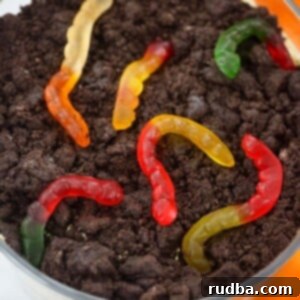 Ultimate Oreo Crumble Delight 2 Close-up of a beautifully layered Oreo dirt cake in a trifle bowl, showcasing crushed cookies, creamy pudding, and vibrant gummy worms.