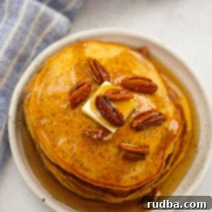 a stack of sweet potato pancakes with pecans, butter, and maple syrup.