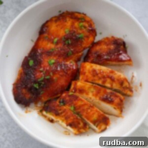 One whole air fryer BBQ chicken breast and one sliced chicken breast on a plate, ready to be served.