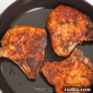Three bone-in pan-seared pork chops in a cast iron skillet.