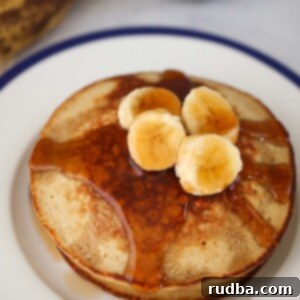 Banana Oatmeal Pancakes 2 A stack of banana oatmeal pancakes with sliced bananas and maple syrup on top.