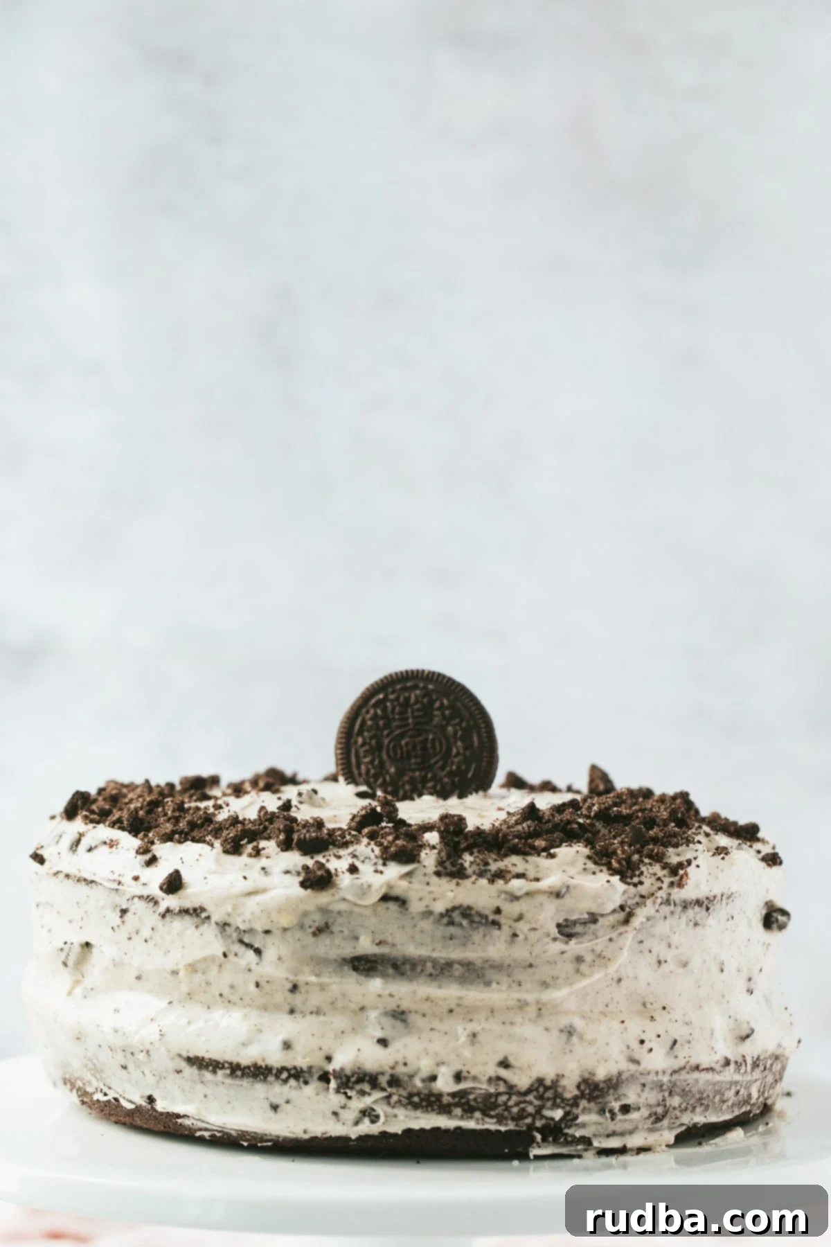 A beautifully layered Oreo cake with a single Oreo cookie on top and crushed crumbs around the sides, set against a light background.