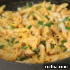 A close-up of a delicious plate of Buffalo Chicken Pasta, garnished with fresh green onions.
