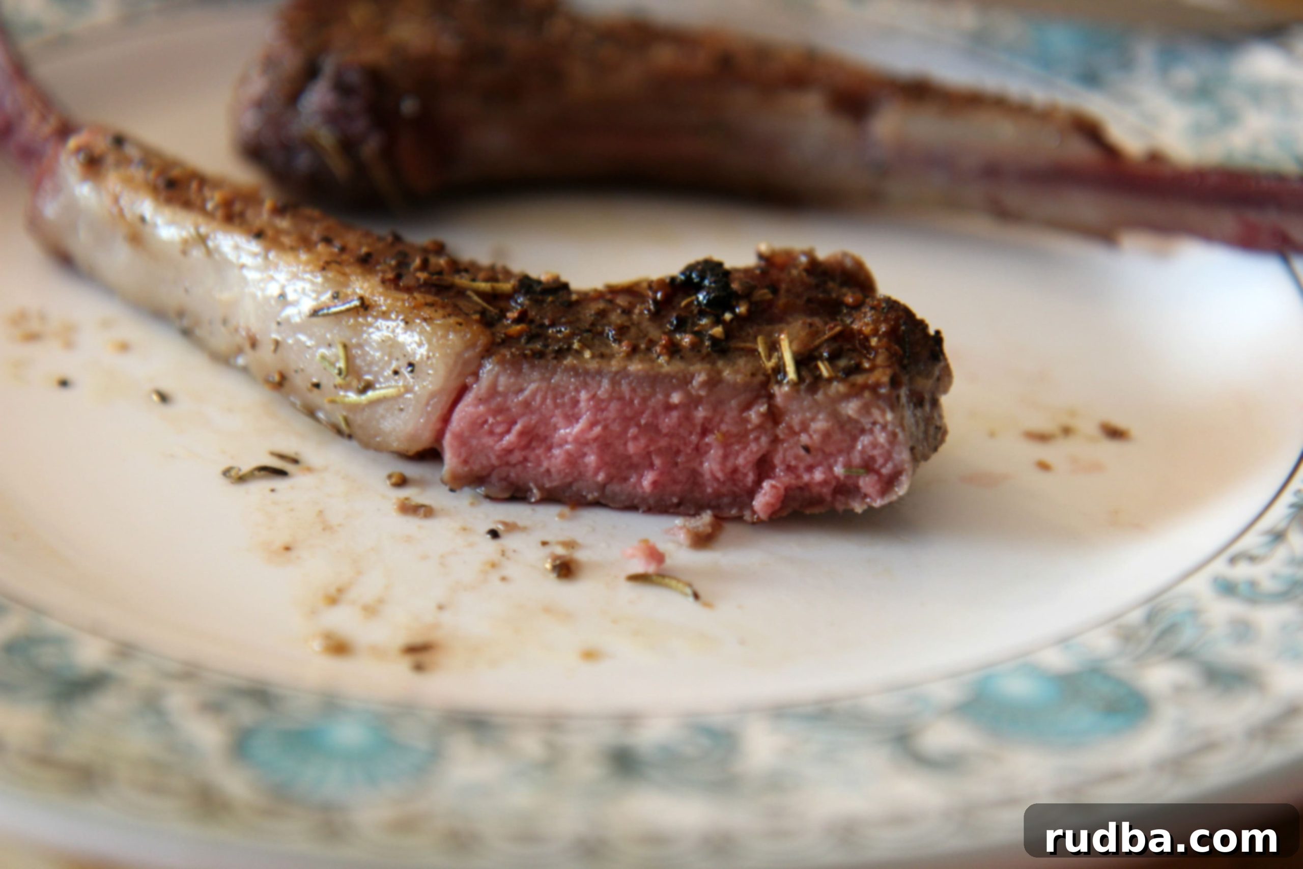 A close-up of a medium-rare cooked lamb chop, showing the pink center and juicy texture.