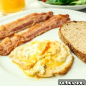 A perfectly cooked over medium egg with two strips of crispy bacon and golden brown toast, ready for a delicious breakfast.