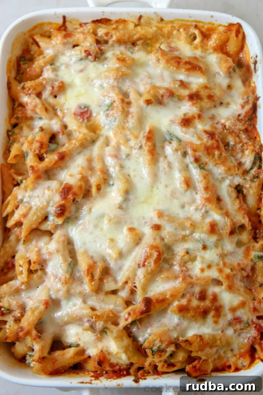 baked ziti with spinach and melted mozzarella cheese on top in a white casserole dish. 