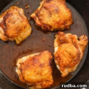 Four pan-seared chicken thighs in a cast iron skillet.