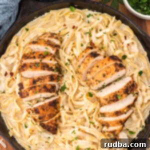Creamy Chicken Fettuccine 2 chicken fettuccine alfredo in a black skillet with red pepper flakes and parmesan cheese on the side.