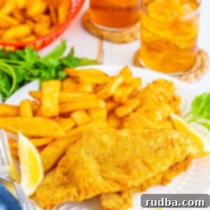 Two Southern fried catfish fillets with fries on a plate and lemon wedges on the side.
