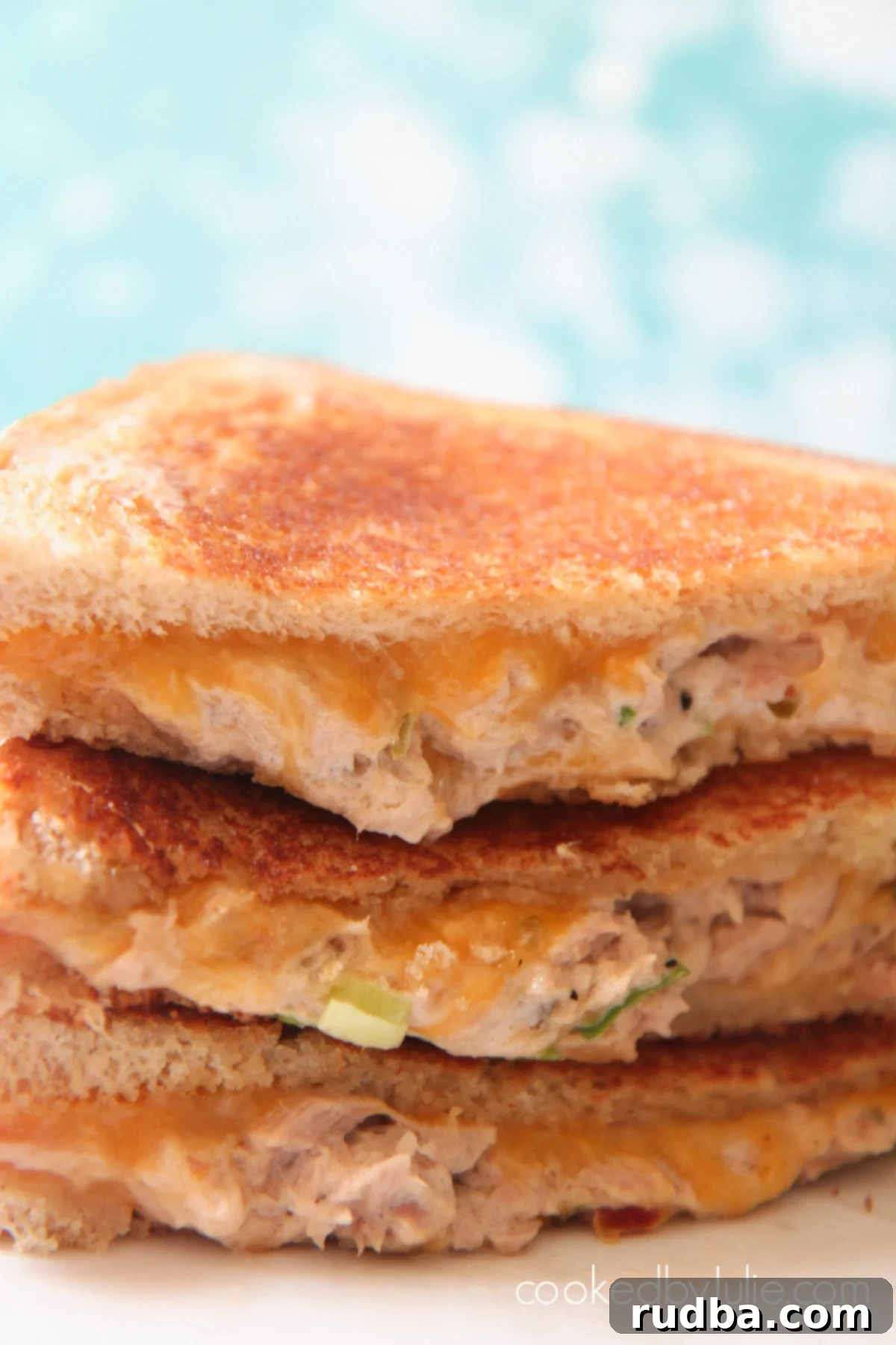 Three tuna melt sandwiches displayed closely, showcasing their golden crust and melted cheese, against a blue backdrop.