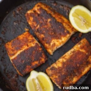Three perfectly seasoned and seared blackened mahi mahi fillets with lemon wedges on the side.