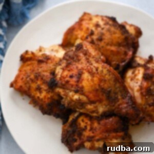 Roasted chicken thighs on a white plate, garnished with fresh herbs.