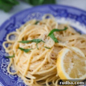 creamy lemon spaghetti on a blue plate with a lemon slice on the side.