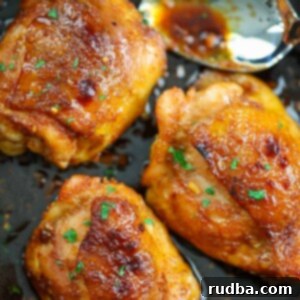 Sticky Honey Garlic Chicken Thighs 2 Three honey garlic chicken thighs in a skillet with a spoon.